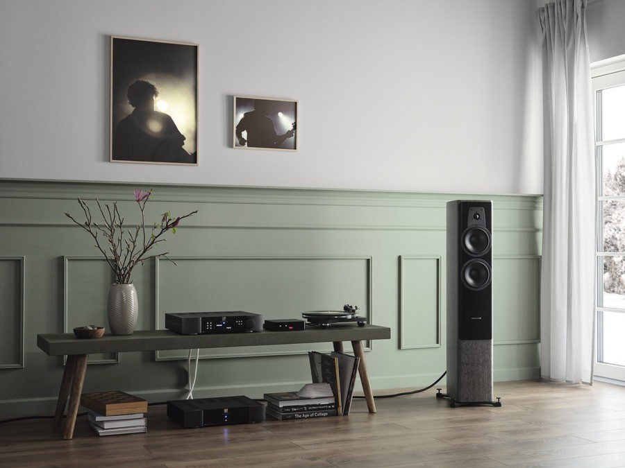 Modern hi-fi setup with turntable and streamer on wooden console, black floor-standing speaker, and mint green wainscoting walls