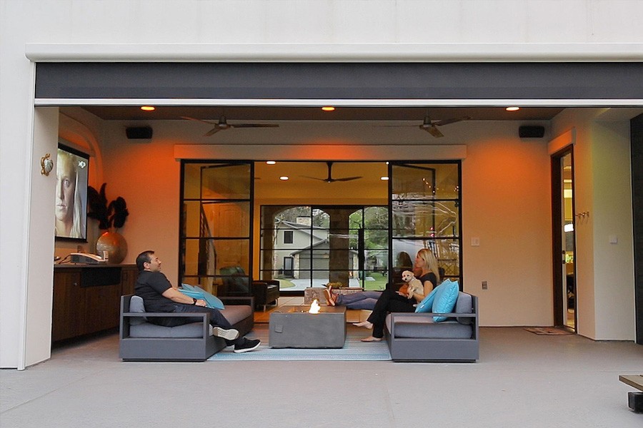 A couple sits enjoying their outdoor patio space with a sofa, TV, and outdoor fans.