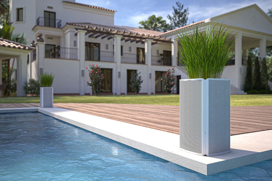 Stylish outdoor Coastal Source planter with integrated speaker design placed beside a luxury pool, with a large modern villa and manicured lawn in the background.