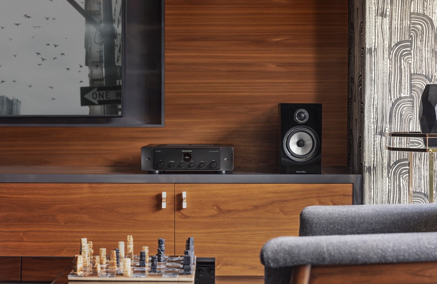 A Marantz AV receiver on a shelf beside a bookshelf speaker and under a TV. 
