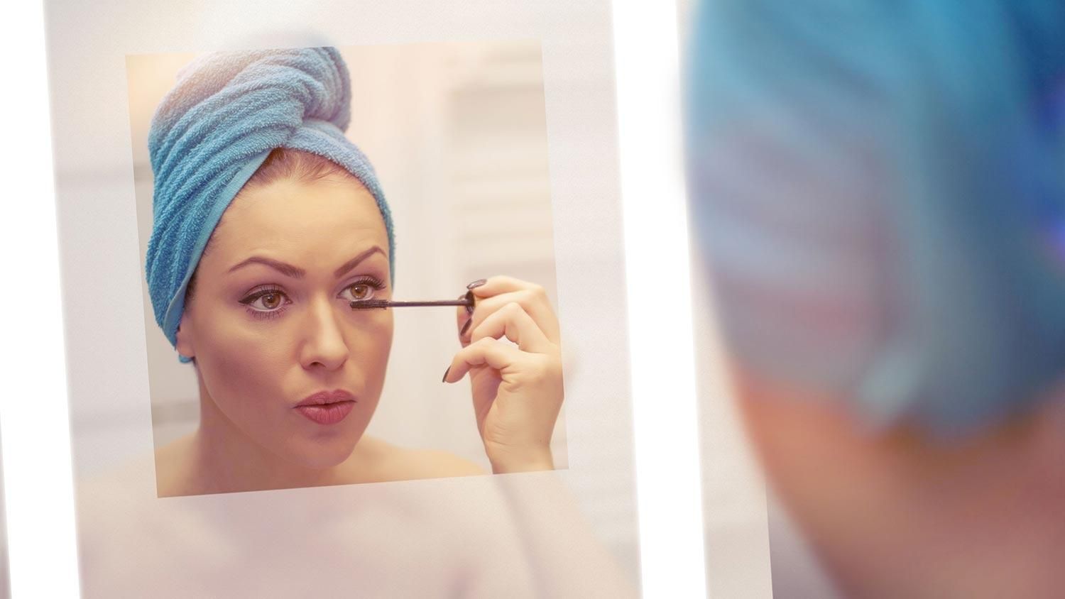 Woman doing her makeup with thanks to the defogger technology in a Seura Mirror