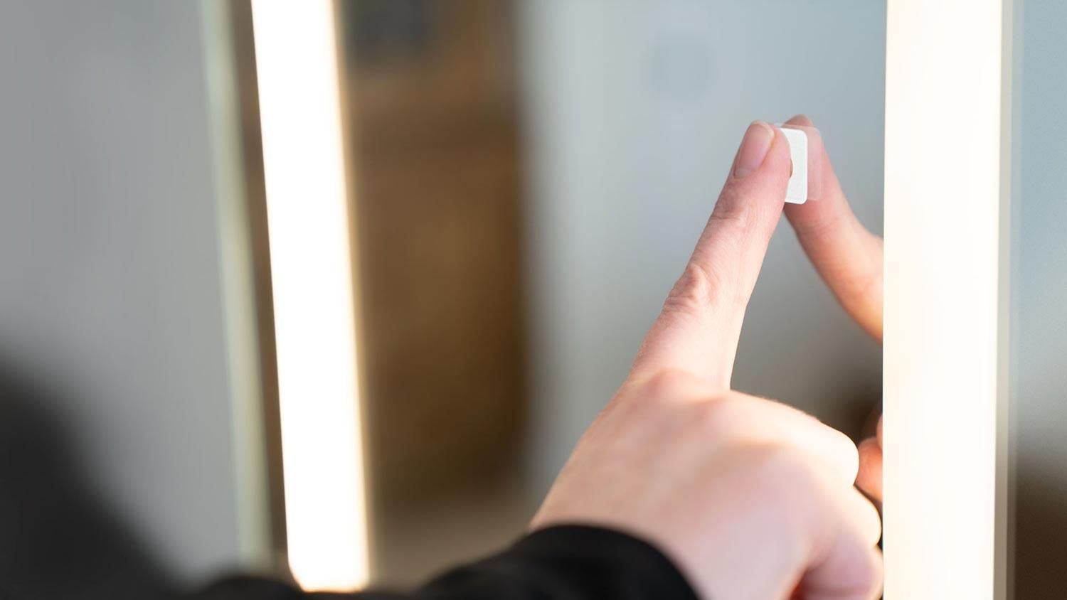 Woman's hand touching the Seura Touch Control Upgrade in a mirror